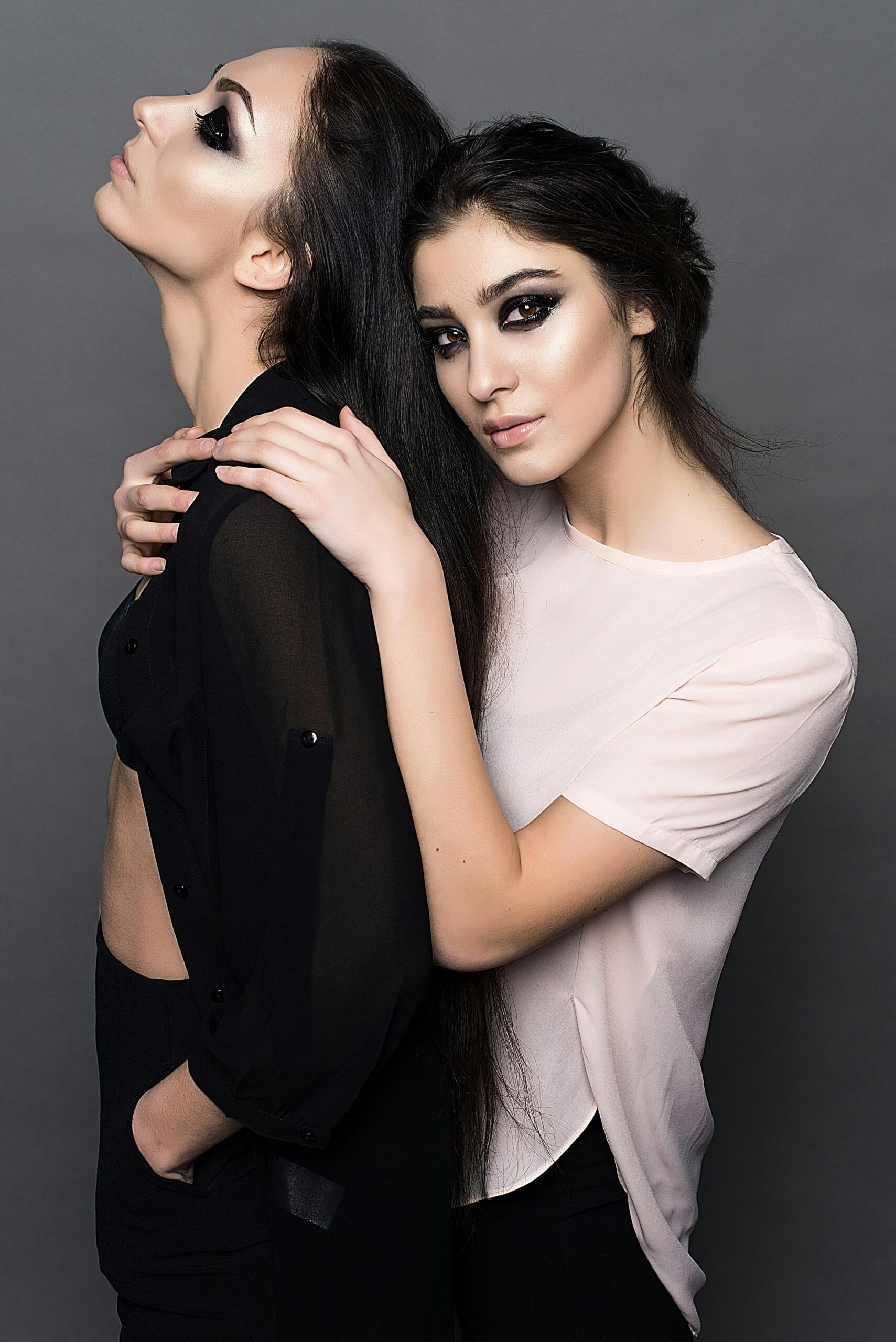 Stylish portrait of two women showcasing makeup and fashion in a studio setting.